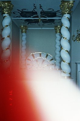 Vintage interior shot featuring ornate blue-and-gold striped columns framing a grand staircase. Circular skylight above revea...