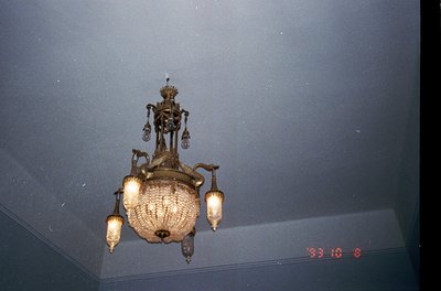 Vintage ornate chandelier with Art Nouveau-inspired metalwork and glass lanterns, mounted on a textured ceiling. Likely from ...