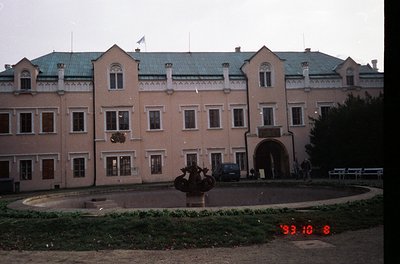 Neoclassical building with symmetrical façade, featuring arched windows and a central entrance. Prominent statue in circular ...