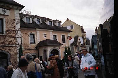 Vintage European street scene featuring a bustling crowd near a **1970s-era hotel** with "N" signage. Ivy-covered façade, gab...