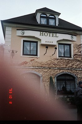 Vintage 35mm photo of a European-style hotel façade with ivy-covered walls, arched windows, and a peaked roof. Decorative clo...