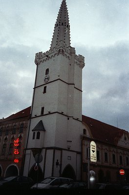 Historic Gothic-style tower with pointed spire, likely a church or town hall, featuring crenellated upper sections and a coat...