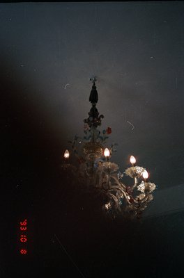 Vintage close-up of ornate chandelier with intricate metalwork, floral motifs, and warm bulbs. Dark, moody lighting enhances ...