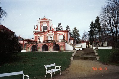 Baroque-style pavilion with red-and-white striped brickwork, central dome, and arched colonnades. Overgrown park setting with...
