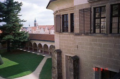 Historic courtyard view of a stone building with arched colonnades, likely a monastery or cloister. Gothic-style church spire...