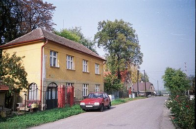 Vintage 1980s-era residential street with Soviet-era architecture: two-story yellow building featuring red garage doors and w...
