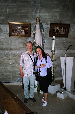 Two individuals pose indoors in a chapel-like setting, likely Eastern European (1990s). The man wears a floral shirt and jean...
