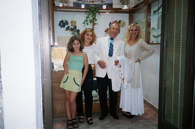 Family portrait in formal attire, likely a wedding or celebration, featuring four individuals: a young girl in a green strapl...