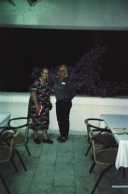 Two women pose outdoors at night under artificial lighting, likely a resort or hotel patio. The elder woman wears a patterned...