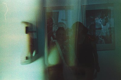 Vintage Polaroid-style photo through a frosted glass door, revealing a blurred indoor scene with a woman in a patterned dress...