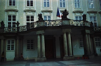 Neoclassical courtyard facade featuring ornate balustrade with sculpted urns, flanked by tall Corinthian columns. A flagpole ...