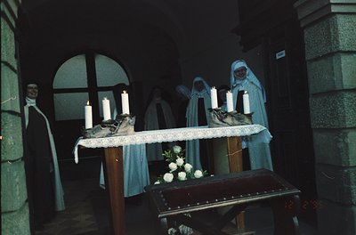 Religious procession altar featuring nuns in traditional habits, holding lit candles. Wooden lectern draped in white cloth wi...