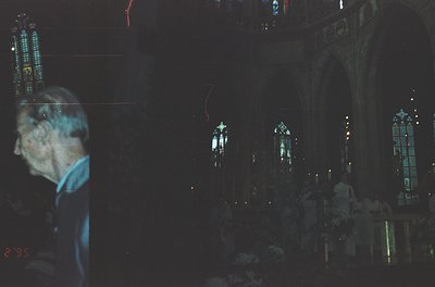 Blurred silhouette of a person in a blue shirt inside a dimly lit Gothic-style church, illuminated by stained-glass windows c...