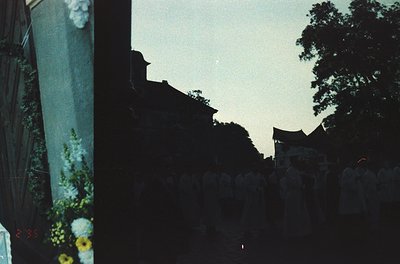 Vintage Polaroid-style shot of a dimly lit alleyway framed by a white picket fence and lush greenery. Sunlight filters throug...