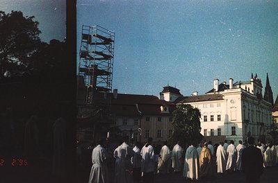 Vintage sepia-toned photo of a formal procession in a European courtyard, likely 1950s–1960s. Uniformed men in long coats mar...