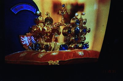 Elaborate crown adorned with gold filigree, sapphires, and emeralds, displayed under dramatic lighting. Intricate heraldic de...