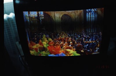 Vintage film strip projection of a packed concert hall, featuring a large orchestra and audience in a grand, arched interior....