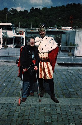 Vintage photo of two individuals in medieval-inspired attire on a cobblestone plaza, likely from the 1970s–1980s. The man wea...