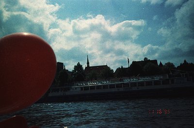 Vintage photo of a river scene with a red buoy in foreground. Historic European riverside buildings and a church spire frame ...