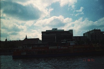 Vintage urban riverside scene with mid-20th century architecture. Prominent brick building with "Marina" signage, likely a ho...