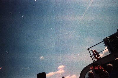Vintage aerial shot of a clock tower displaying **12:30**, framed by a vintage camera lens. The hazy sky suggests mid-20th-ce...