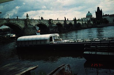 Vintage bus ferry crossing Prague’s Charles Bridge (), 1960s-70s. Iconic Gothic towers and statues frame the historic stone a...