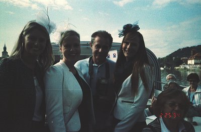 Four individuals pose on a boat in a lakeside urban setting, likely Zurich, Switzerland, judging by the architecture and sign...