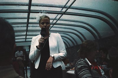 Vintage indoor concert shot featuring a performer holding a microphone in a dimly lit, curved-roof venue. Audience wears retr...