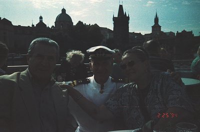 Vintage group photo in Prague’s Old Town, featuring 1960s-era attire (men in suits, women in patterned dresses). Iconic skyli...