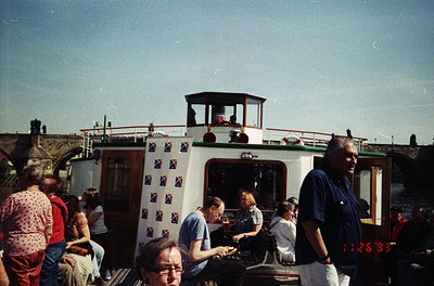 Vintage narrowboat with British flag-patterned trim, docked in a canal setting. Crowd of casually dressed passengers on deck,...