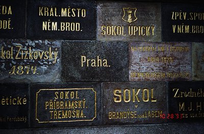 Weathered bronze plaques on a stone wall, inscribed with Czech/German text and dates. Notable entries: "Praha," "Sokol Upický...