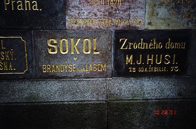 Vintage brass plaque on stone wall: "SOKOL BRANDÝS NAD LABEM" (Czech gymnastic/social club) with "Zrodného domu M.J. Husi" (b...