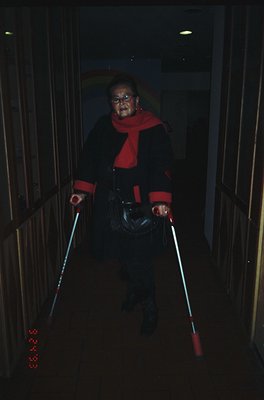 Portrait of an elderly individual descending stairs using illuminated canes, likely for mobility assistance. Dark coat with r...