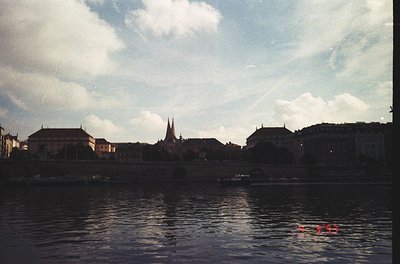 Vintage waterfront scene featuring a serene river reflecting historic European architecture. Prominent brick buildings with p...