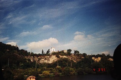 Vintage Polaroid-style shot of a coastal lighthouse perched on rocky terrain, surrounded by dense greenery. The timestamp "Y ...
