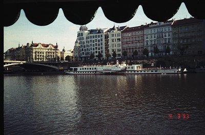 Vintage 1960s Prague riverside scene featuring the iconic **Dvořák Bridge** in foreground. Mid-century architecture includes ...