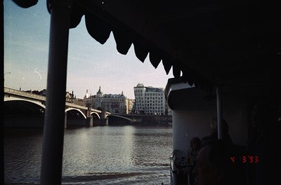 Vintage shot of a river scene framed by a boat’s scalloped edge, likely the Danube. Historic stone bridge and mid-century mod...
