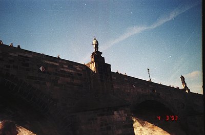 Vintage black-and-white shot of Prague’s Charles Bridge, featuring a statue atop a stone balustrade. Gothic architecture with...