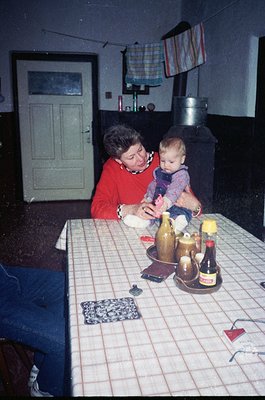 A woman in a red sweater interacts with a baby at a table covered with a checkered tablecloth, surrounded by vintage bottles ...