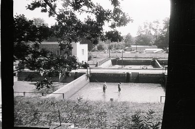 Black-and-white snapshot of a flooded residential courtyard, likely mid-20th century. Two children wade through shallow water...