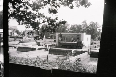 Vintage black-and-white photo of a mid-20th century courtyard featuring a low-rise, modernist building with flat roof and min...