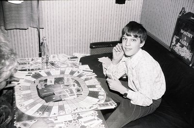 Young boy in 1970s-era home playing board game with circular layout, surrounded by scattered game pieces. Mid-century interio...