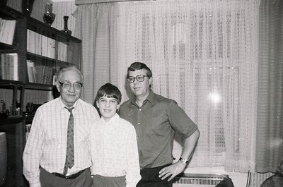 Three individuals pose indoors in a mid-century setting: an older man in a striped tie, a young boy in a button-down, and ano...