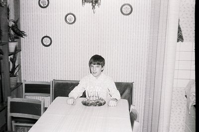 Mid-century kitchen interior with vertical striped wallpaper and round wall sconces. Young boy seated at a rectangular table,...