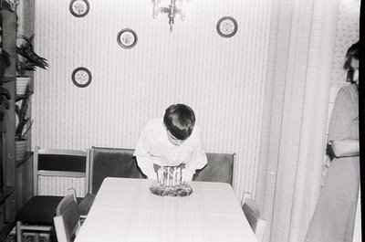 Mid-century dining scene with child seated at round table, back to camera. Plain wallpaper, circular wall decorations, and vi...
