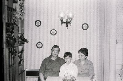 Vintage black-and-white family portrait featuring three generations: a man in a dark shirt, a boy in a white shirt with a lit...