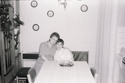 Mid-20th century indoor portrait: two individuals seated at a small round table in a modestly furnished room, likely 1960s–19...