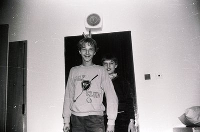 Two boys pose indoors, likely in a 1970s-1980s setting. The boy on left wears a "Golf Club" sweatshirt with a logo, while the...