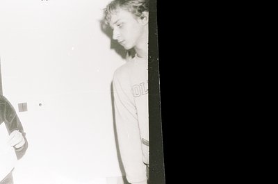 Vintage black-and-white photo of two individuals in a dimly lit indoor setting, likely a 1970s–1980s home or studio. One pers...