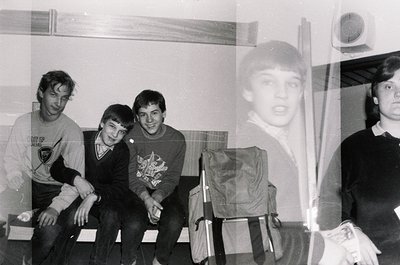 Four young men pose indoors, likely a school or dormitory setting, mid-1970s. Left to right: one wears a sweatshirt with a lo...